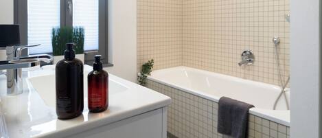 A modern bathroom with a white sink, two bottles of toiletries, a bathtub, and a shower.