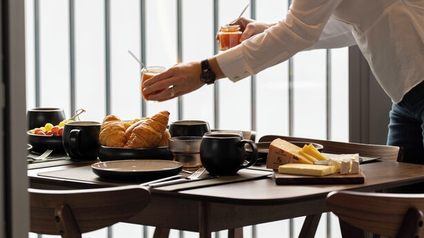 A breakfast table with croissants, cheese, and coffee cups.