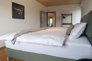 A neatly made bed with white linens and a green headboard, a wooden bunk bed in the background, and a bull painting on the wall. - The Adress Zurich- Your stylish temporary home (Wettingen)