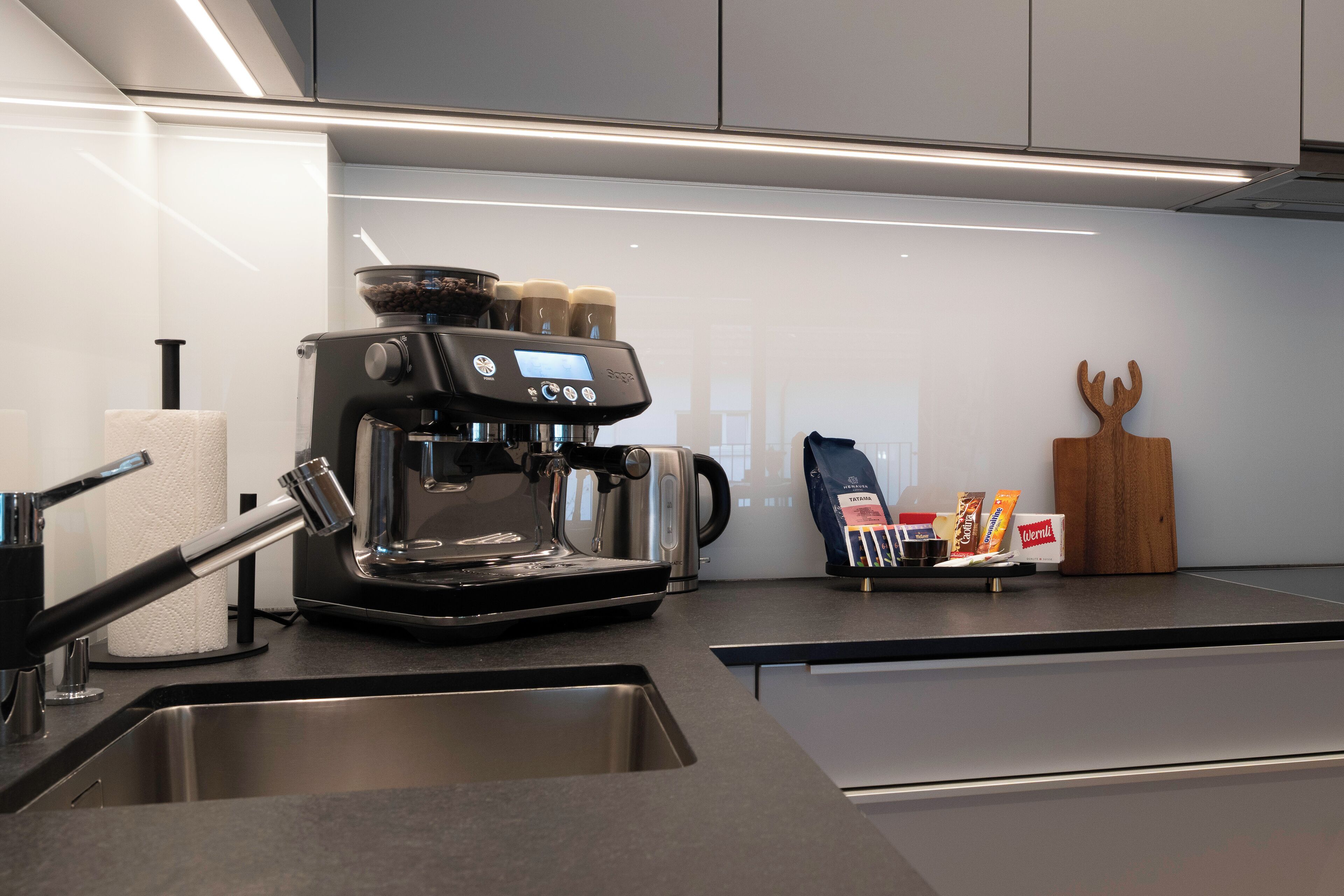 Eine moderne Küche mit integrierter Kaffeemaschine, einer Spüle aus Edelstahl und einem Holzer Schneidebrett.