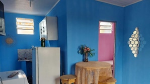 A room with blue walls, a white refrigerator, a wooden table with a lace tablecloth, and two wooden stools. - House, 2 bedrooms with air conditioning, airy, fully equipped. (Salvador)