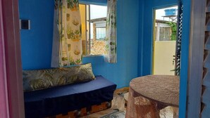 A room with a blue wall, a bed with a patterned pillow, a small table, and a window with curtains. - House, 2 bedrooms with air conditioning, airy, fully equipped. (Salvador)