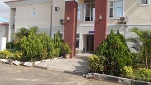 A building with a beige facade, red pillars, and a paved entrance area with potted plants. - Pine Crest Hotel and Suites  (Abuja)
