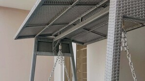 A wicker swing chair with a blue cushion, suspended by chains from a metal frame. - Pine Crest Hotel and Suites  (Abuja)