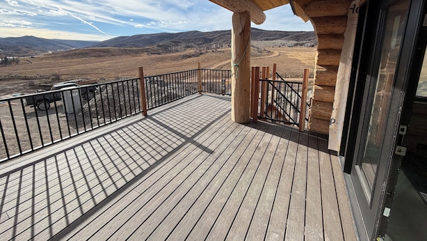 Eine Holzterrasse mit Metallgeländer, mit Blick auf eine gebirgige Landschaft.
