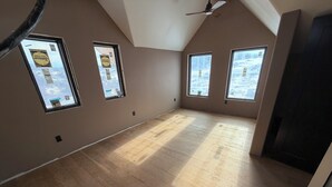 Ein Zimmer mit schräg verlaufender Decke, Holzboden und drei Fenstern.