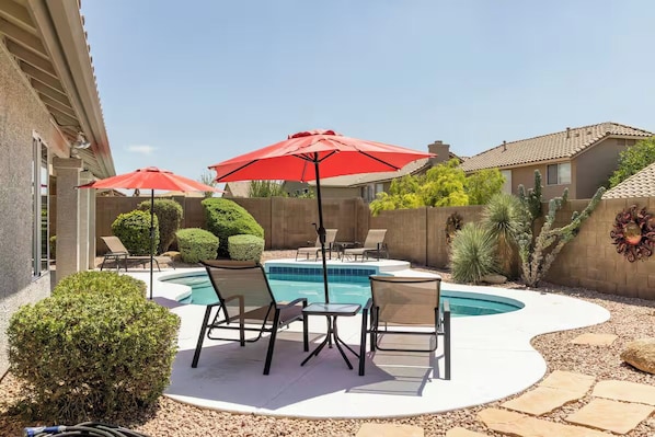 Un jardin avec une piscine, des chaises longues et des parasols rouges.