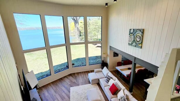 A spacious living room with a large window overlooking a body of water, a built-in fireplace, and a cozy seating area. - Lake Gervais Retreat: Castle House - Dock and Sauna (Saint Paul)
