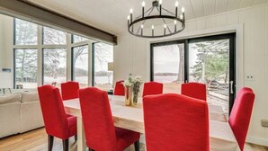 A dining area with a wooden table and red chairs, large windows, and a chandelier. - Lake Gervais Retreat: Castle House - Dock and Sauna (Saint Paul)