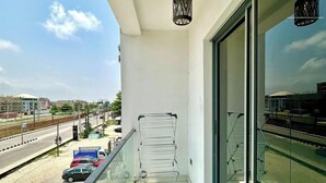 A balcony with a metal rack, a hanging light fixture, and a view of a road and buildings. - Zustel Hotel (Enugu)