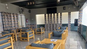 A seating area with wooden furniture and grey cushions, a tiled wall with a brick pattern, and a ceiling fan. - Zustel Hotel (Enugu)