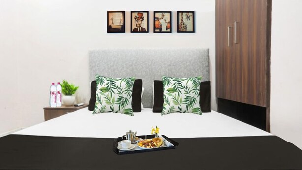 A neatly made bed with a black bedspread, two pillows with a leaf pattern, and a tray with breakfast items. - Hotel S Grand (Prayagraj)