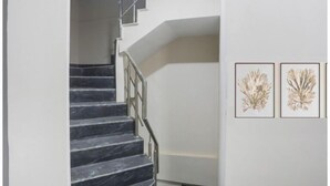 A staircase with a metal railing leading to a landing. Two framed botanical prints are displayed on the wall. - Hotel S Grand (Prayagraj)