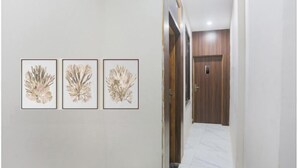 A hallway with three framed botanical prints on the wall, a wooden door at the end, and a tiled floor. - Hotel S Grand (Prayagraj)