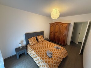 A bedroom with a bed, a nightstand, a wardrobe, and a door. - Biscarrosse apartment in town center, 10 minutes from the ocean and 5 minutes from the lake (Biscarrosse)
