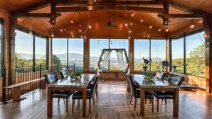 Un comedor espacioso con mesas y sillas de madera, ventanas amplias que ofrecen vistas a la montaña, y luces colgantes en el techo.