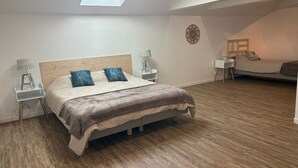 Ein Schlafzimmer mit Dachfenster, einem Bett mit Holz-Kopfteil, zwei Nachttischen mit Lampen, einem Beistelltisch und einem kleinen Schreibtisch mit Stuhl.