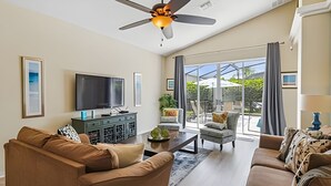 Un amplio salón con ventilador de techo, televisor de pantalla plana y un ventanal con vistas al exterior.