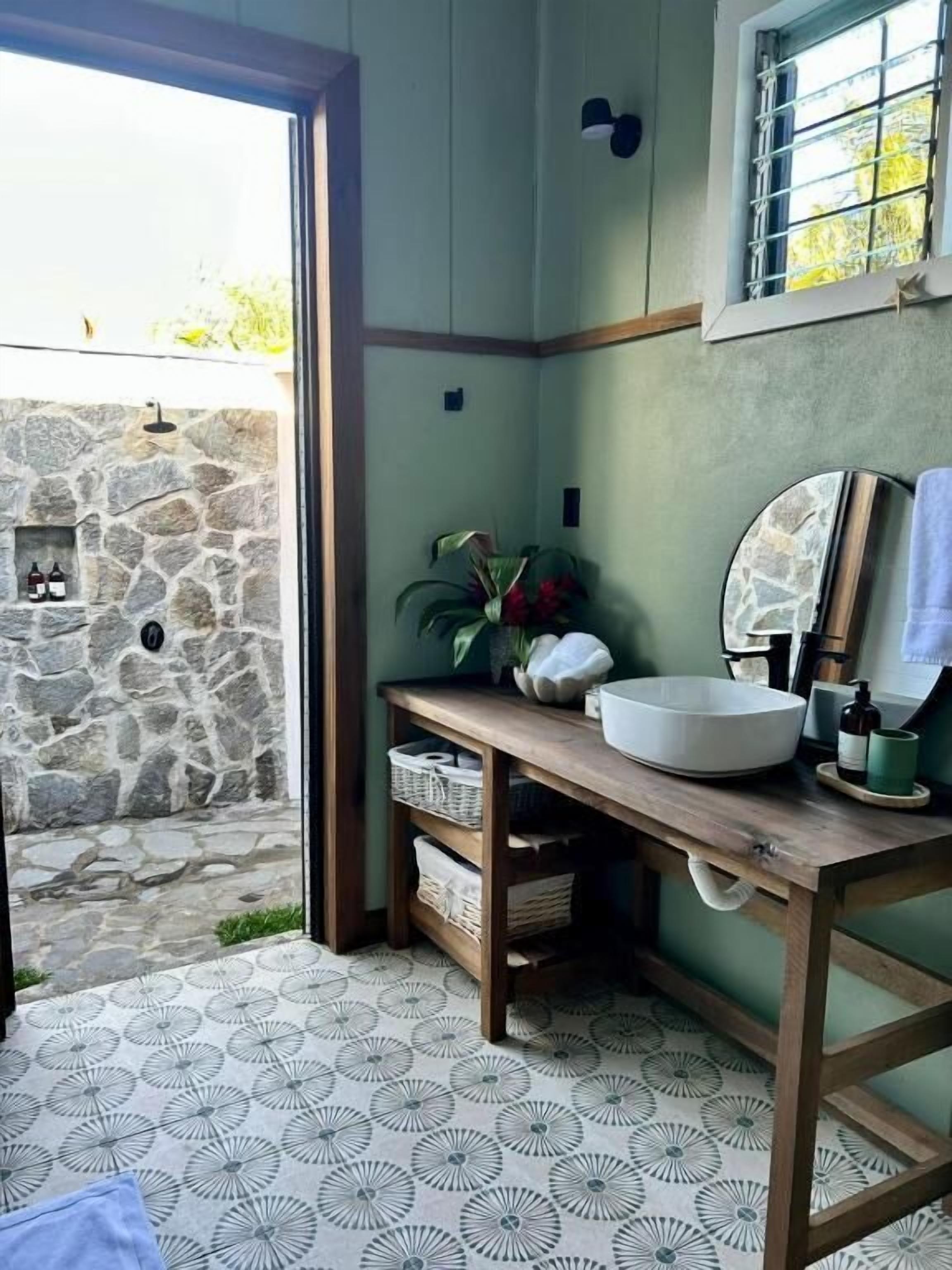 A bathroom with a stone wall, a wooden vanity, a sink, and a window with a view of the outside.