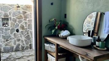 A bathroom with a stone wall, a wooden vanity, a sink, and a window with a view of the outside.