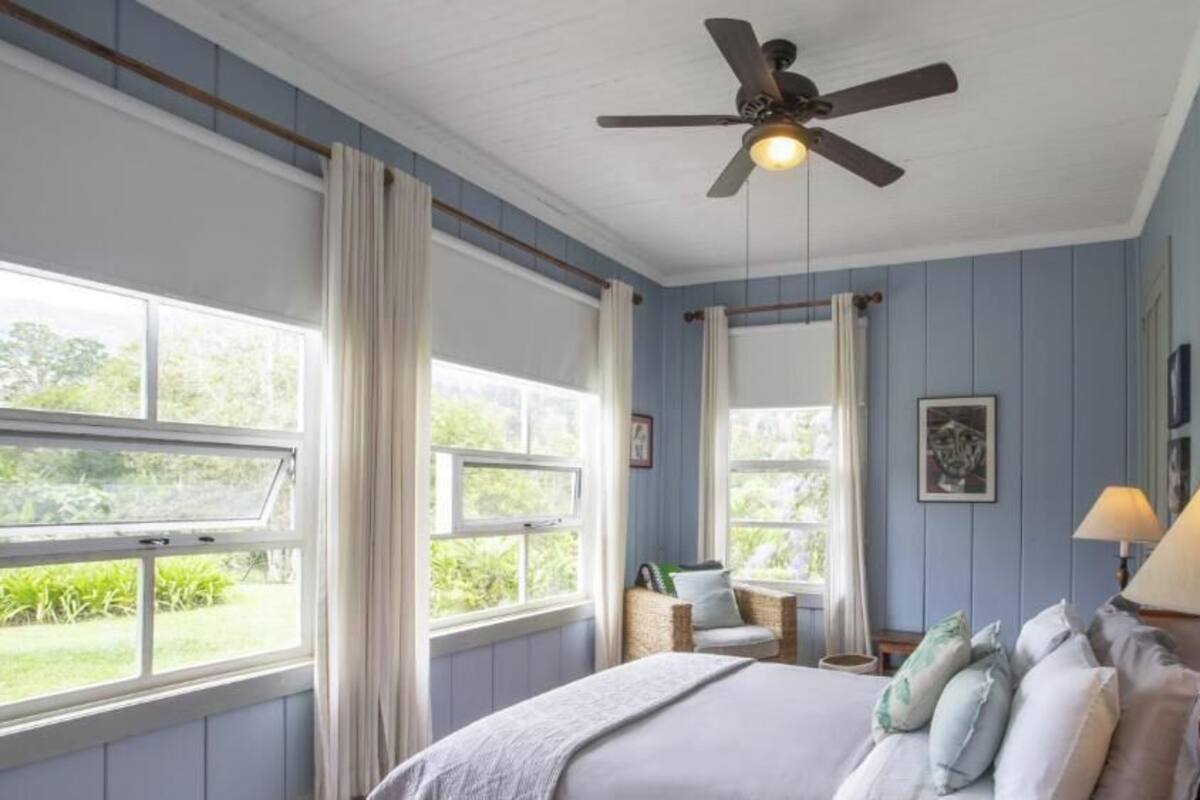 Ein Schlafzimmer mit Bett, zwei Nachttischlampen, einem Deckenventilator und Blick ins Freie.