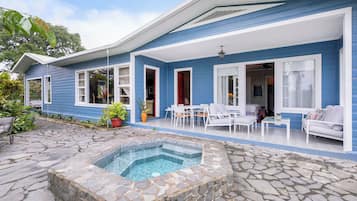 A blue house with a stone patio, a swimming pool, and outdoor furniture.