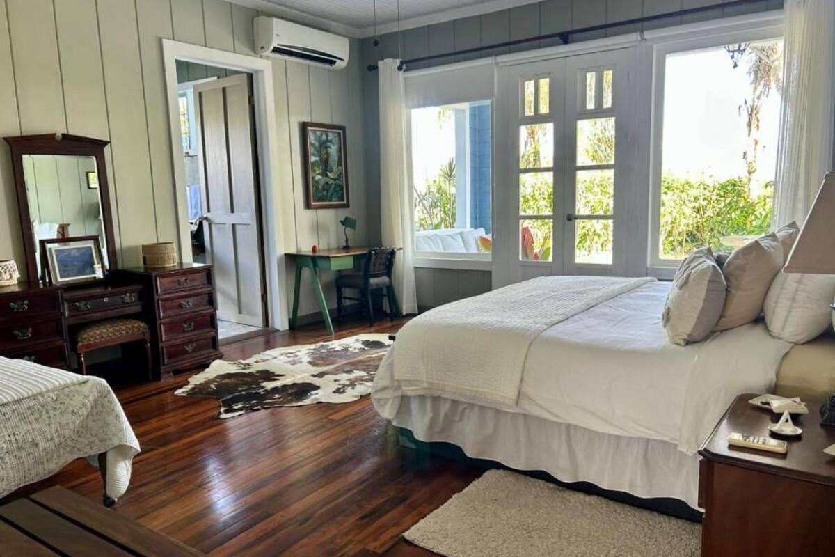 Ein Schlafzimmer mit einem großen Bett, Holzboden, einem Schreibtisch und einem Fenster mit Blick ins Grüne.