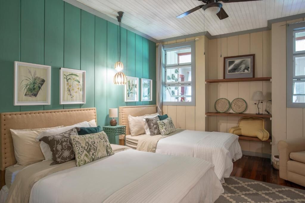 A bedroom with two beds, teal walls, and a ceiling fan.
