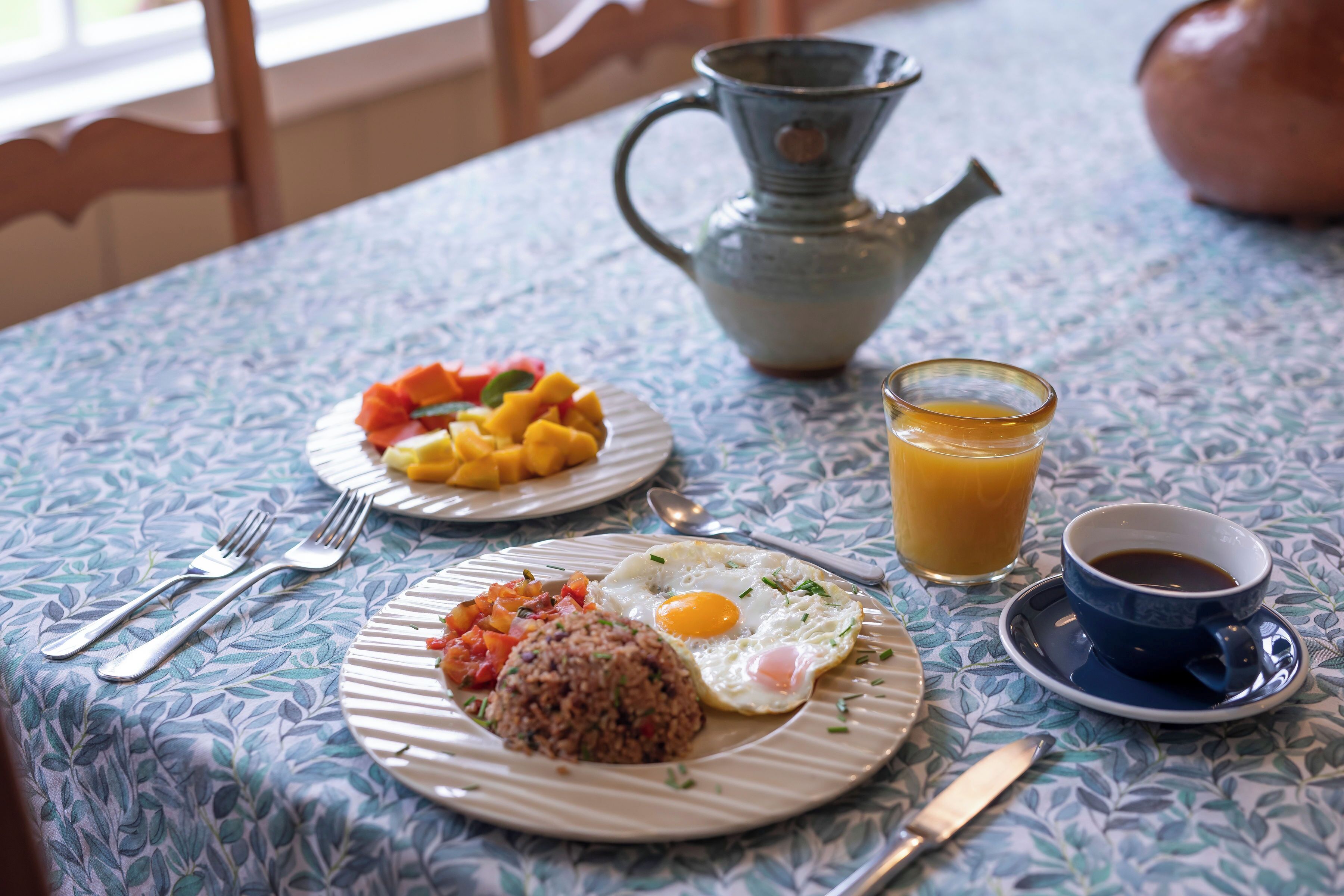 Desayuno servido con platos de comida, una jarra, un vaso de jugo de naranja y una taza de café.