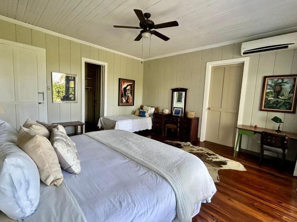 A bedroom with a large bed, a ceiling fan, a dresser, and a desk with a chair.