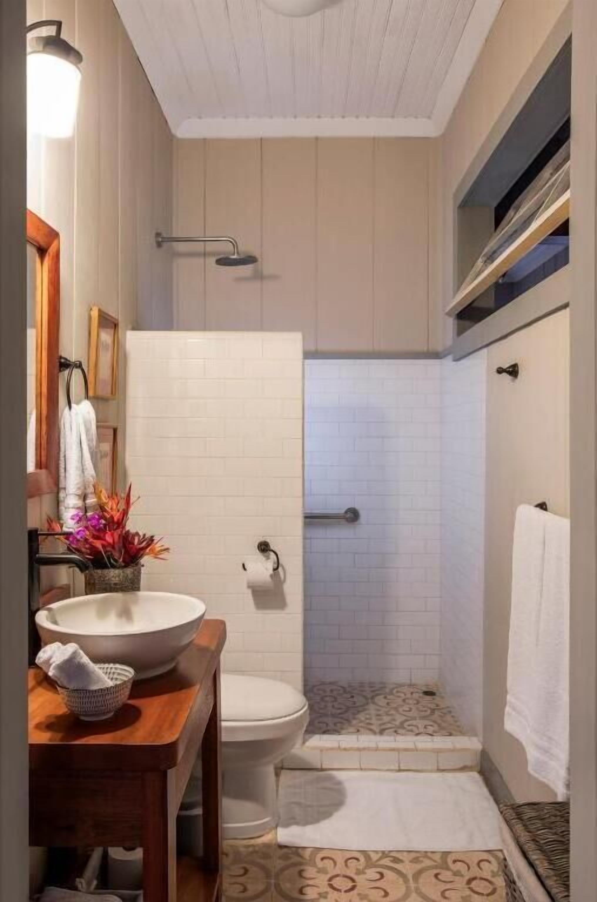 Un baño compacto con tocador de madera, un lavamanos grande, inodoro y zona de ducha.