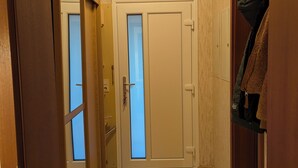 Ein Flur mit Holzboden, einer Doppeltür mit satinierten Glasscheiben und einem Kleiderständer mit Jacken.