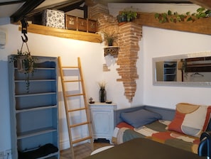 Una habitación con cama de altillo, escalera de madera, pared de ladrillo y una planta colgante.