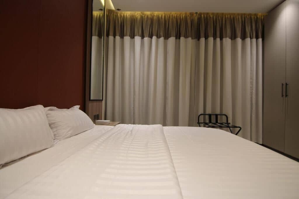 A hotel room with a large bed, a nightstand, a chair, and a wardrobe.
