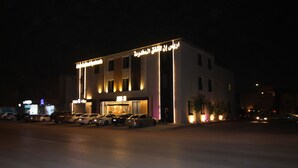 A building with illuminated signage and parked cars in front. - Aris in Apartment (Riyadh)