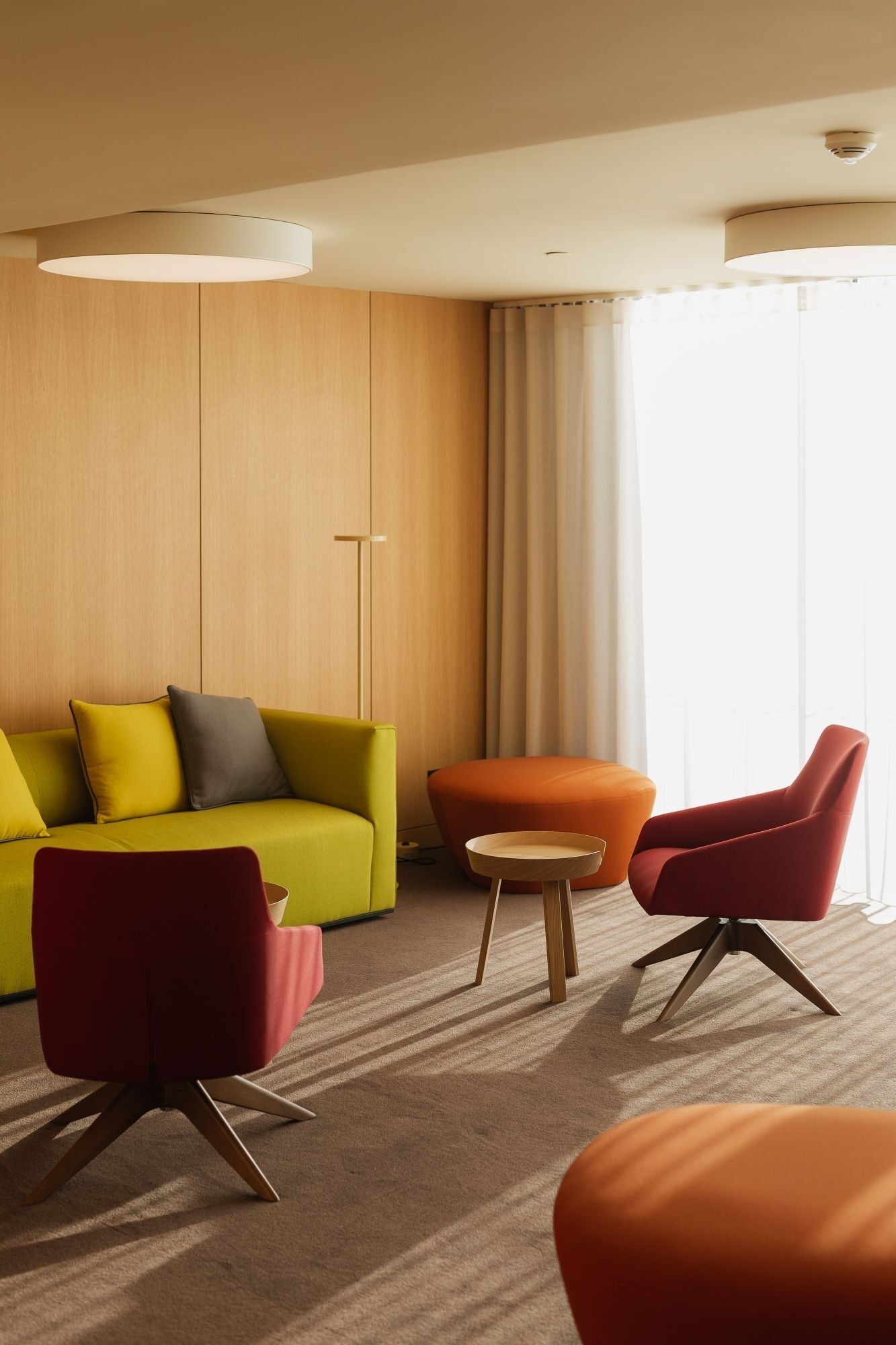 Ein modernes Hotelzimmer mit einem gelben Sofa, roten Sesseln und einem kleinen Holztisch.