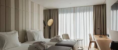 A hotel room with two beds, a desk, a chair, and a large window with curtains.