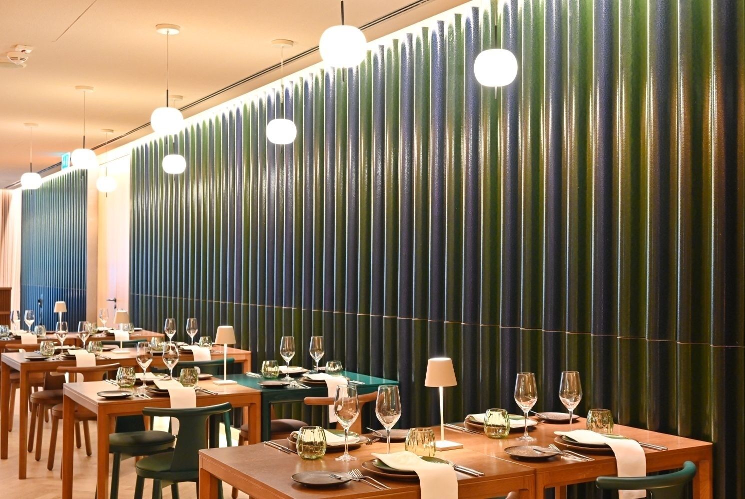 A restaurant with multiple tables set for dining, featuring a unique vertical bamboo-like wall design.
