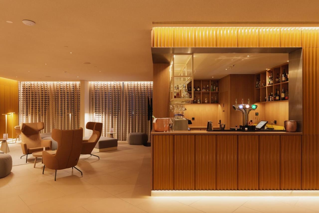 Un espace bar moderne avec un comptoir d’accueil en bois, un coin salon avec des chaises et un bar bien visible, où sont exposées de nombreuses bouteilles.