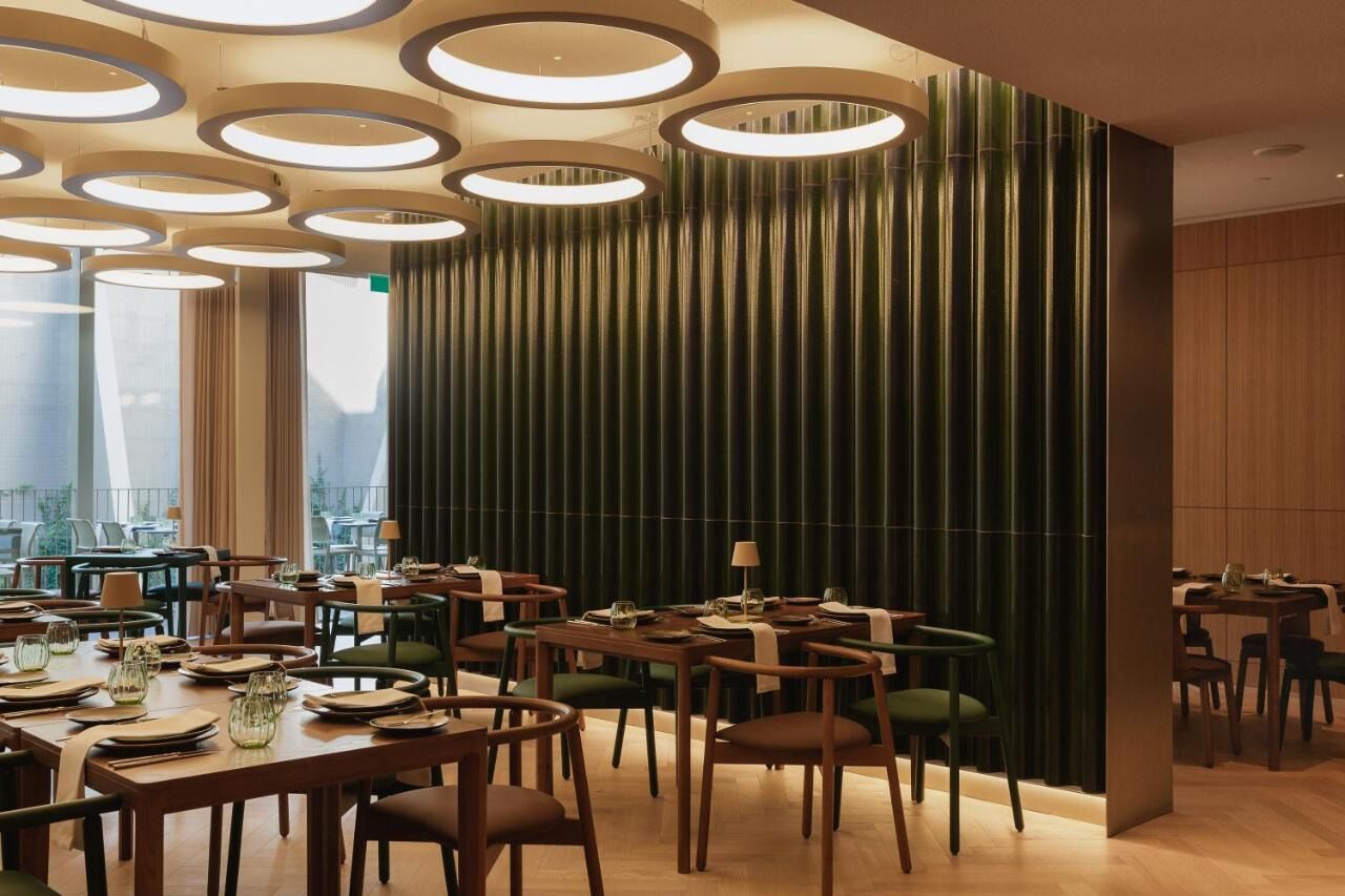 A modern restaurant with round ceiling lights, wooden tables, and green chairs.