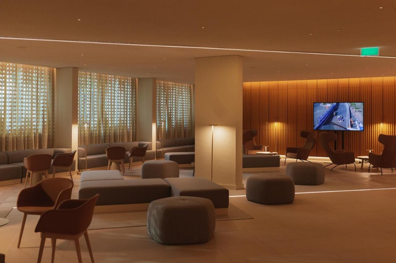 Un espace de détente moderne, doté de canapés, de poufs et de fauteuils, d’un téléviseur à écran plat et d’une grande fenêtre avec des stores verticaux.