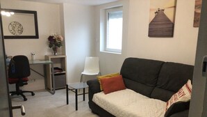 En moderne stue med en mørkegrå sofa, et lille hvidt bord, et glas skrivebord, en hvid stol og et indrammet kunstværk på væggen.