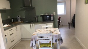 Et lille køkken med lyse skabe, en mikrobølgeovn og en komfur. Et spisebord med stole er placeret i midten.