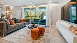 A modern living room with a grey sofa, orange ottomans, a coffee table, and a large TV on a white console. - (Davenport)