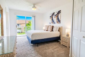 Ein Schlafzimmer mit einem Bett, einem Glastisch, einem Nachttisch, einem Deckenventilator und Blick ins Freie.