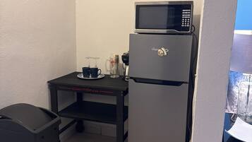 Una kitchenette equipada con refrigerador, microondas y un letrero de café en la pared.