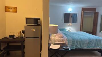 Een compacte kamer met een kitchenette, een bed, een bureau en een bordje 'COFFEE'.