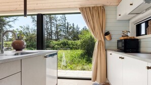 A modern kitchen with a large window, a hanging light fixture, a microwave, and a rustic kettle on the counter. - "Afkar" - 900m from the sea by Interhome (Løkken)