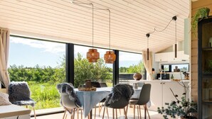 A modern dining area with a table set for four, wooden flooring, and large windows offering a view of greenery. - "Afkar" - 900m from the sea by Interhome (Løkken)