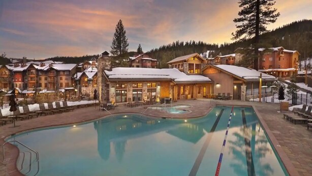 Un resort con piscina, sillones de descanso y edificios de techos nevados.